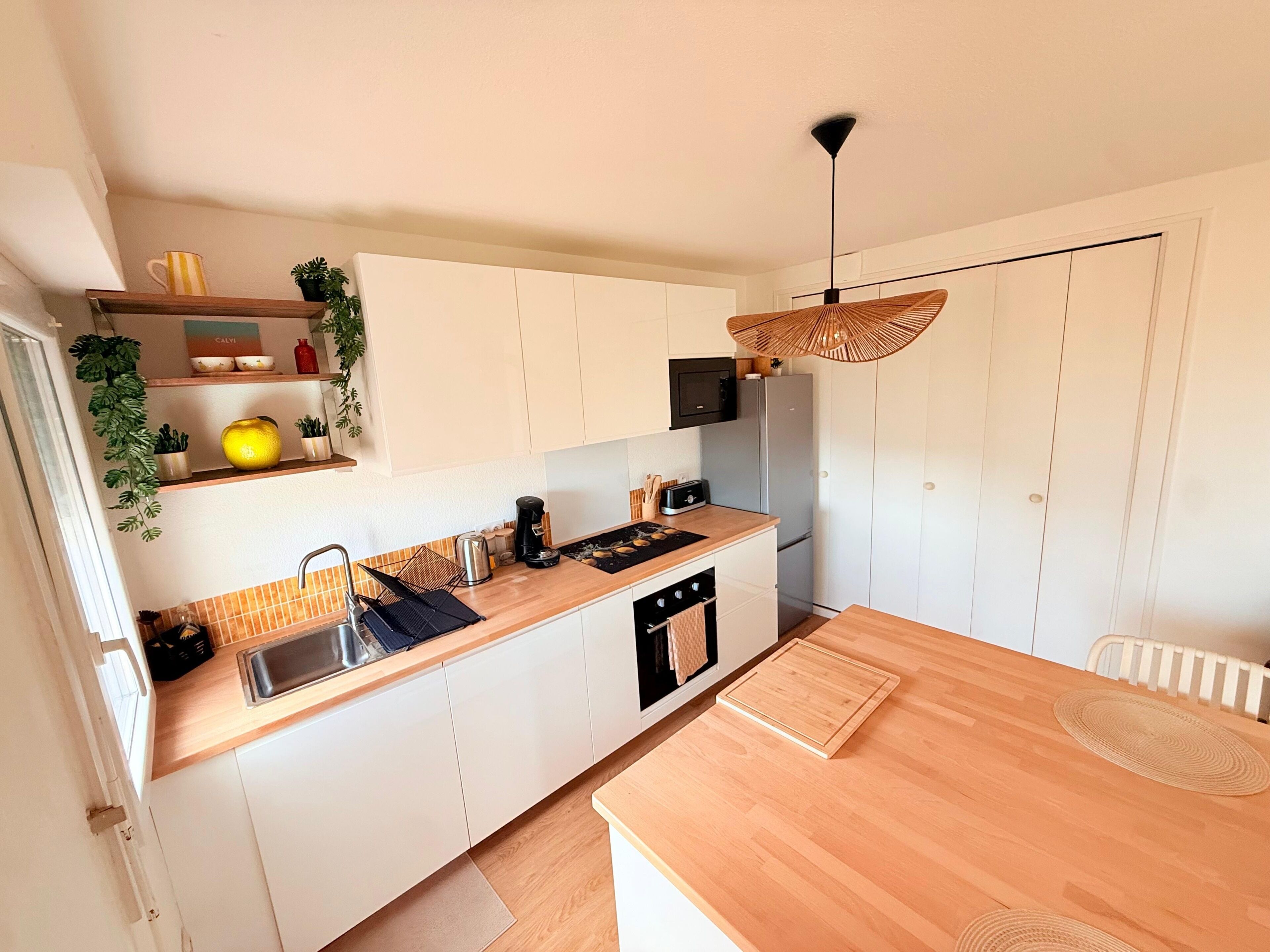 A modern kitchen with white cabinets, a wooden countertop, a sink, a stove, and a hanging light fixture.