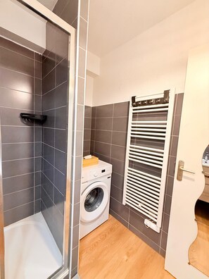 A compact bathroom with a glass shower enclosure, a built-in washing machine, and a towel rack. - A Vacation in the Var: Carqueiranne, the Ideal Town (Carqueiranne)