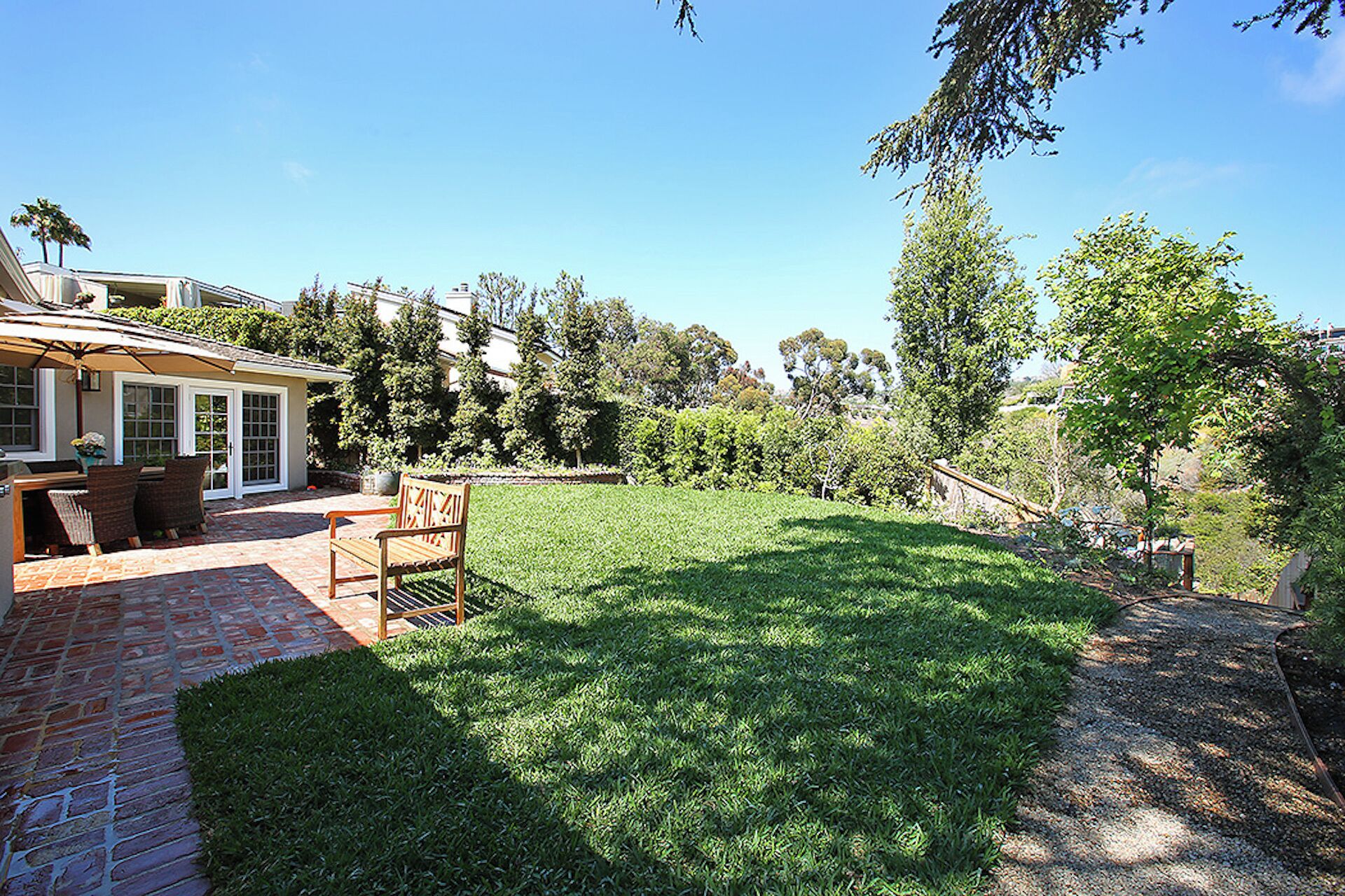 Un jardin avec un espace patio, un banc en bois et une pelouse.