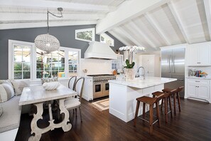 A kitchen with a central island, wooden bar stools, a dining table with chairs, and a chandelier. - Gorgeous 3-bedroom home in beautiful CDM with AC and backyard (Newport Beach)