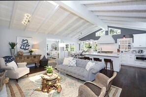 A spacious living room with a grey sofa, a coffee table, and a dining area with a kitchen in the background. - Gorgeous 3-bedroom home in beautiful CDM with AC and backyard (Newport Beach)
