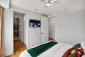 A bedroom with a bed, a green throw blanket, a ceiling fan, and a mounted TV displaying streaming services.