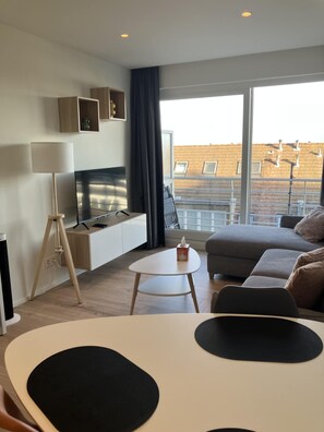 Ein modernes Wohnzimmer mit einer Couch, einem Couchtisch, einem Fernseher und einem Balkon mit Blick.