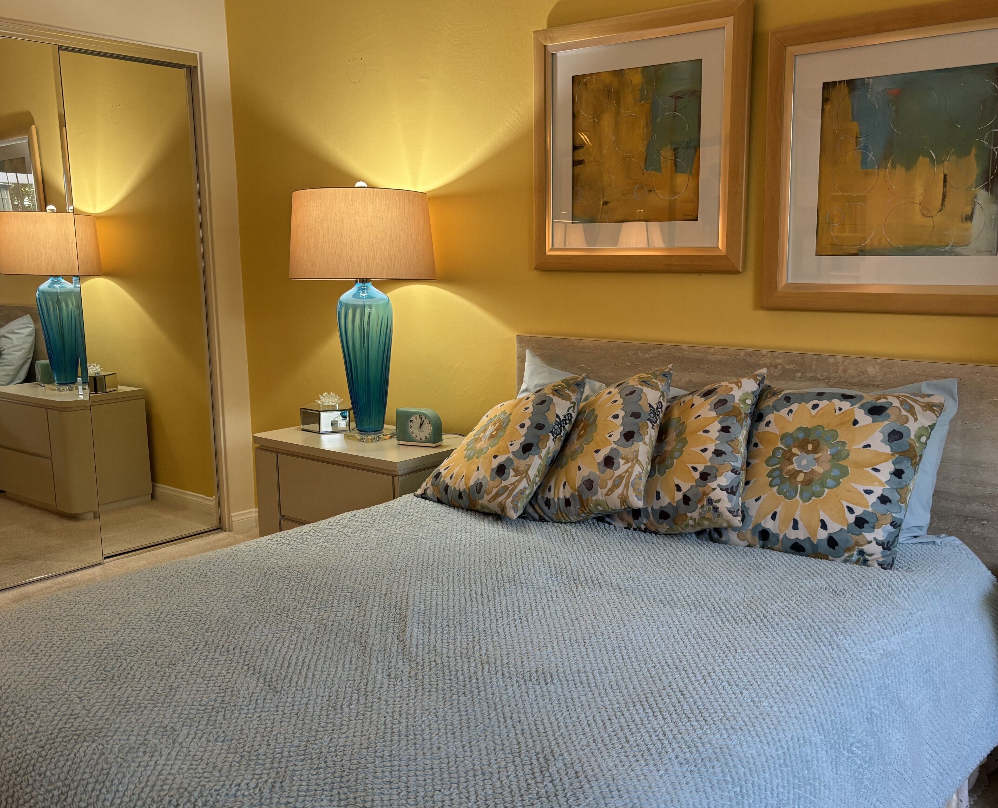 Un dormitorio con una cama, una mesita de noche, una lámpara y dos cuadros en la pared.