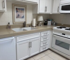 A kitchen with white cabinets, a double sink, a stove, and a framed artwork on the wall. - Winter Specials-Welcome to the Desert Retreat-in the historic Tennis Village (Palm Springs)