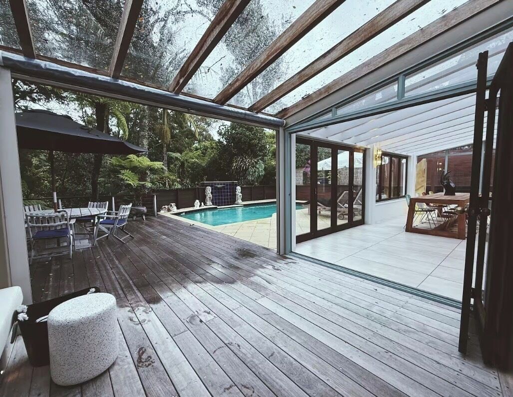 Una terrazza esterna con piscina, pavimento in legno e porte vetrate che danno su un ambiente interno.