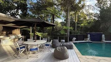 Una terrazza esterna con barbecue, tavolo da pranzo, sedie e zona piscina.