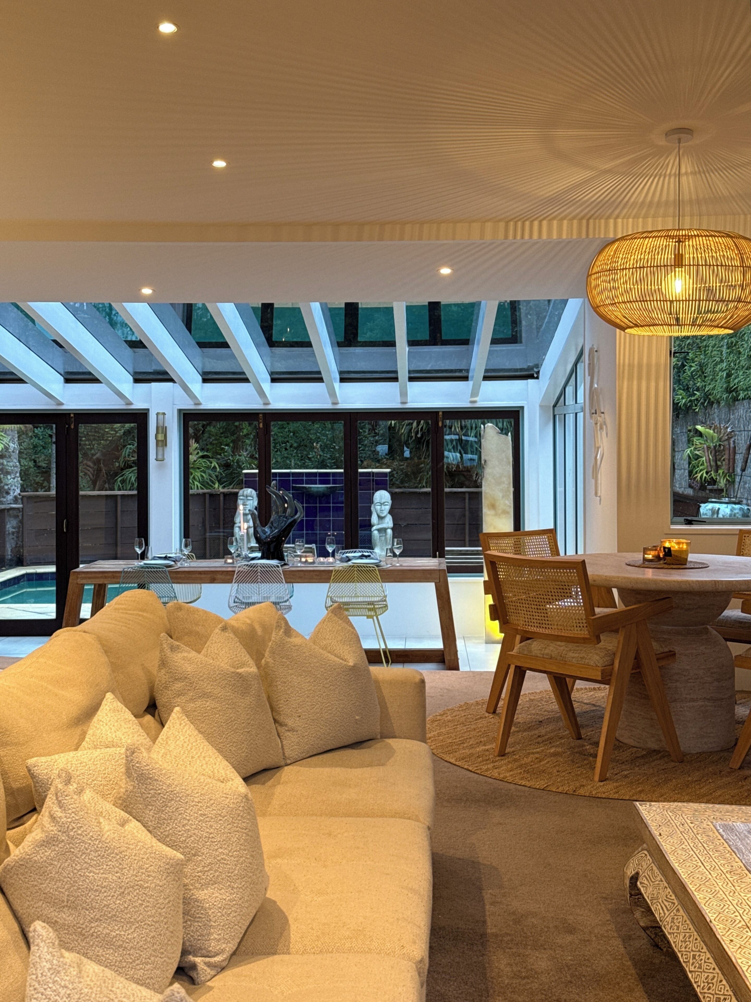 A modern interior with a sofa, dining table, and chairs, a large window, and a hanging light fixture.