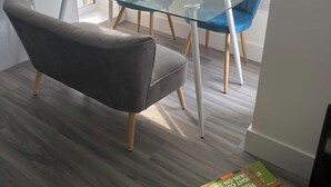 Ein stilvoller Essbereich mit einem Glastisch, zwei blauen Stühlen und einem grauen Sofa.