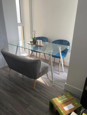 Un espace repas moderne avec une table en verre, deux chaises bleues et un canapé gris.