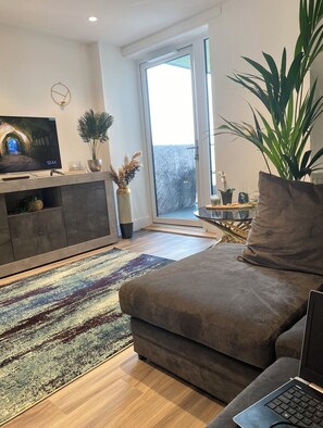 Un salon moderne avec un canapé, un téléviseur, un ordinateur portable et une plante en pot.