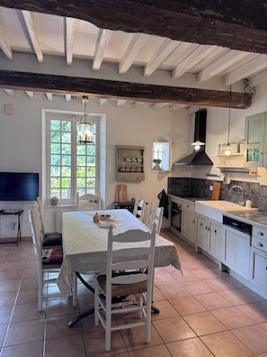 A kitchen with white cabinetry, a dining table with chairs, a window with a view, and a hanging light fixture. - Charming cottage on the Lot River, "Les Tabacs," with a fenced-in private garden. (Clairac)