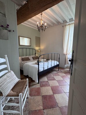 Een slaapkamer met een bed, een stoel, een hanglamp en een raam met gordijnen.