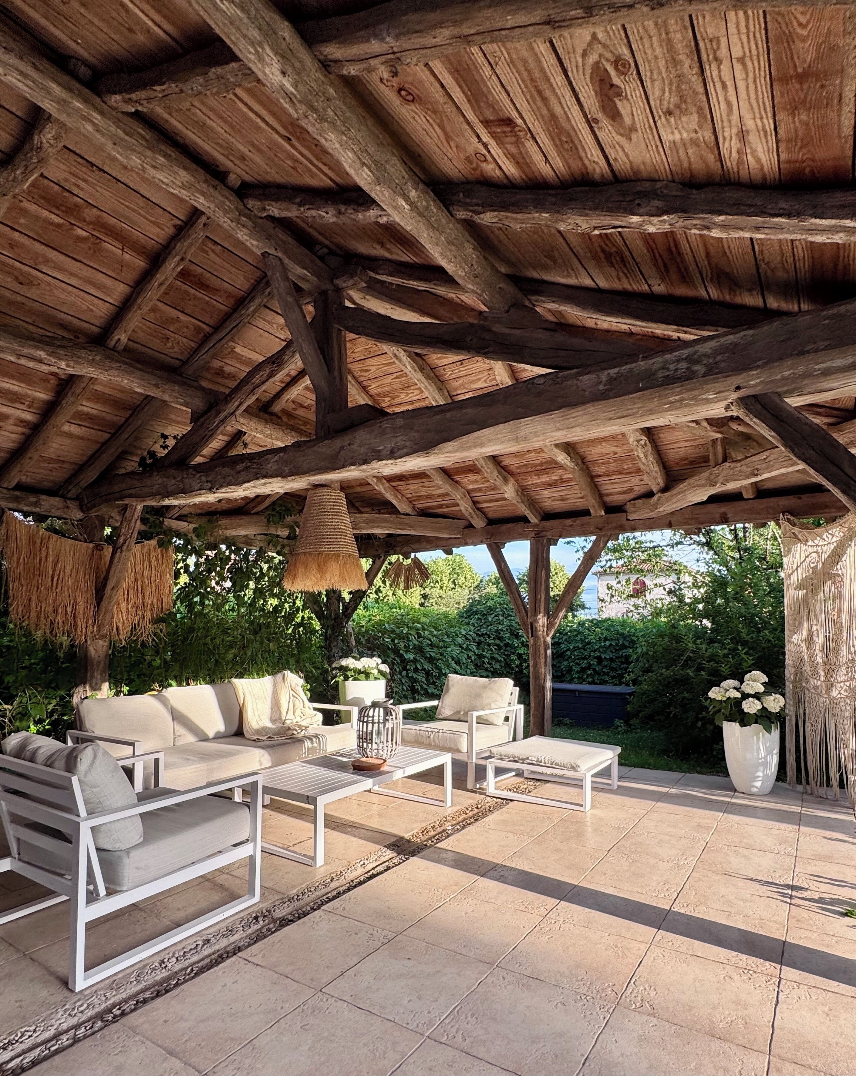 An outdoor patio with wooden beams, a thatched roof, and outdoor furniture.