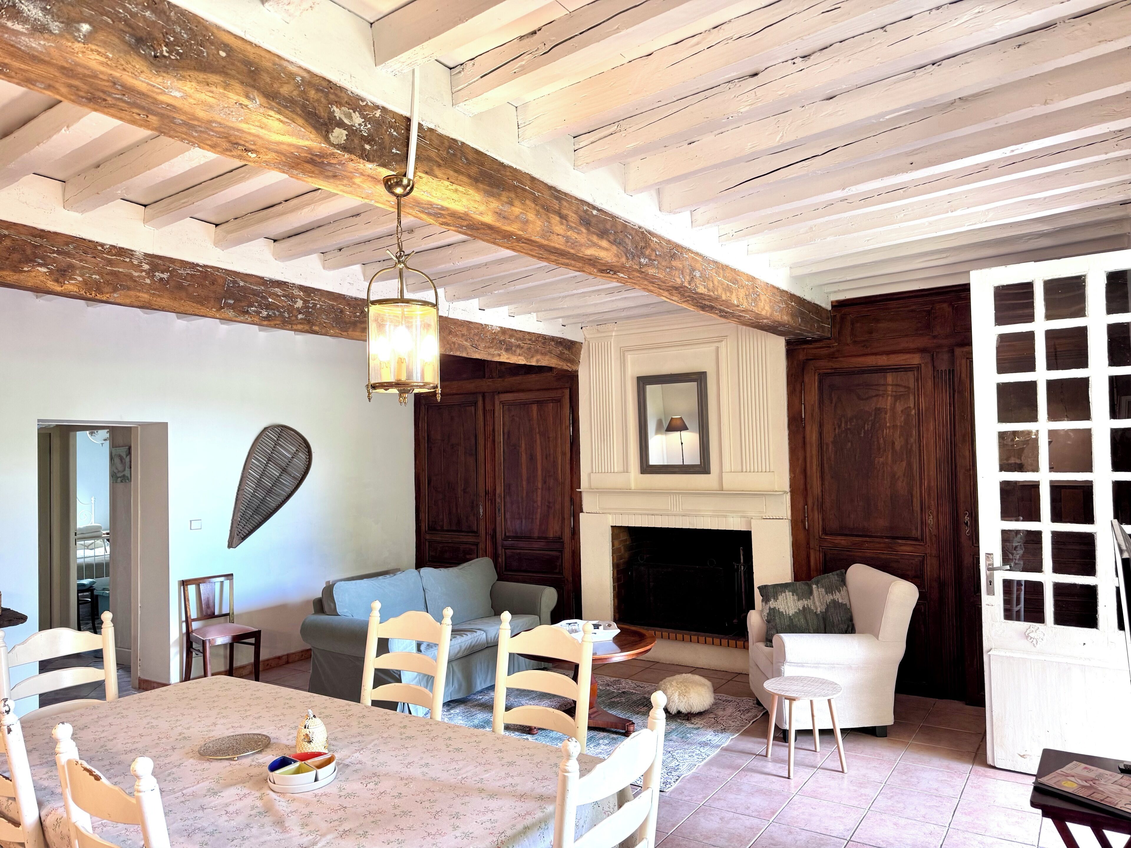 Un salon avec une cheminée, des poutres apparentes, une table à manger avec des chaises et un téléviseur.