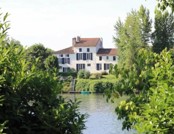 Een groot, wit gebouw met een rood dak, omringd door weelderige begroeiing en een waterpartij.