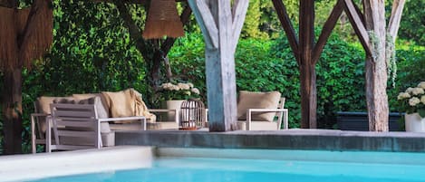 A poolside area with a wooden pergola, lounge chairs, and a table with a vase of flowers.