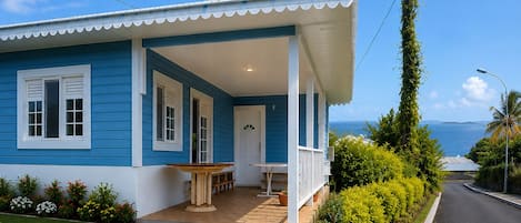 A two-story house with a covered porch, a small table, and a bench.