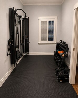 Ett gym med ett svart gummigolv, en träningsbänk och ett ställ med kettlebells.