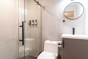 Un baño moderno con ducha de vidrio, inodoro y lavamanos con espejo.