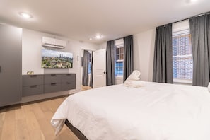 Un dormitorio moderno con una cama grande, un televisor de pantalla plana en la pared y vistas a la ciudad a través de la ventana.