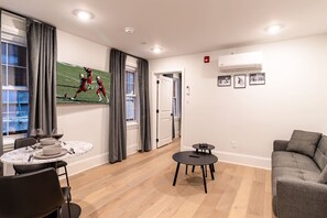 A modern living room with a dining area, a grey sofa, a small round table, and a sports-themed wall art. - Spruce Villa - 3rd Floor King 1BR (Philadelphia)