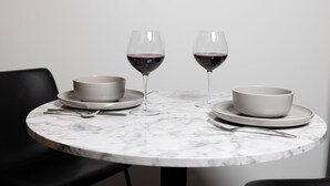 Un tavolo di marmo rotondo con due ciotole bianche, due bicchieri da vino e posate.