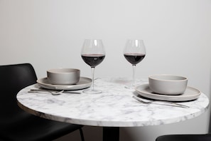Una mesa de mármol redonda con dos cuencos blancos, dos copas de vino y cubiertos.
