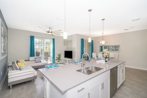 A modern kitchen with a central island, a dining area with a table and chairs, and a living area with a sofa and a television. - Luxury Resort 4BD Home W/Private Pool Near Disney (Kissimmee)