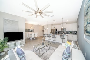A modern living room with a flat-screen TV, a glass coffee table, and a ceiling fan. - Luxury Resort 4BD Home W/Private Pool Near Disney (Kissimmee)