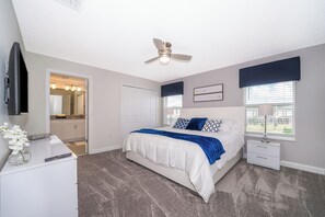 Een slaapkamer met een bed, nachtkastjes, een plafondventilator, een raam met jaloezieën en uitzicht op het omliggende landschap.