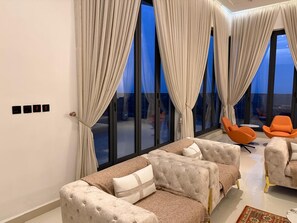 A modern living room with a sofa set, two armchairs, and a large window with curtains. - 3 bedroom all ensuite split level luxury penthouse with skyline views over Abuja (Abuja)