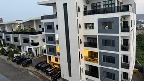 Un immeuble résidentiel à plusieurs étages, doté de balcons, d’un espace de stationnement et offrant une vue sur le paysage environnant.