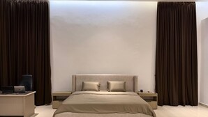 Une chambre à coucher moderne avec un grand lit, deux tables de chevet, un bureau avec un ordinateur portable et des rideaux foncés.