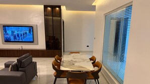 Un salon moderne avec un sol en marbre, une table à manger avec des chaises, un canapé, un téléviseur et une grande fenêtre équipée de stores.