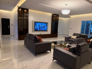 Ein modernes Wohnzimmer mit Fernseher, Sofas und einem Glastisch.