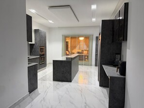 A modern kitchen with a central island, built-in appliances, and a view through a window with blinds. - 3 bedroom all ensuite split level luxury penthouse with skyline views over Abuja (Abuja)