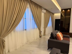 A modern living room with a sofa, curtains, and a large window. - 3 bedroom all ensuite split level luxury penthouse with skyline views over Abuja (Abuja)