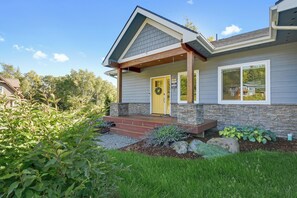 A modern house with a stone foundation, a yellow front door, and a covered porch.