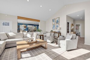 A spacious living room with a large sofa, a coffee table, and a dining area in the background. - Spacious home w full Kachemak Bay views (Homer)