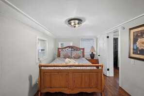 A bedroom with a wooden bed, a bedside table with a lamp, a wall-mounted air conditioner, and a door leading to another room. - Cozy Private 1-BR Ground Unit with Kitchen - 5111A (Tampa)