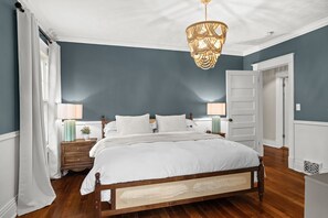 Een slaapkamer met een groot bed, twee nachtkastjes, een hanglamp en een deur.