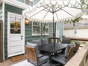 Een buitenterras met een tafel, stoelen, een witte parasol en een rieten mand met sinaasappels.