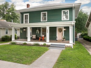 Een huis met twee verdiepingen, een veranda, een voordeur en een kleine voortuin.
