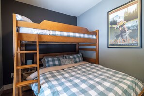 Una cama litera con colcha a cuadros, una escalera y un cartel en la pared.