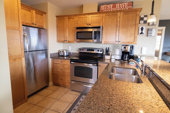 A kitchen with wooden cabinets, stainless steel appliances, granite countertops, and a stainless steel sink.