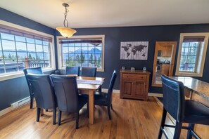 Un comedor con mesa y sillas de madera, una cocina con armarios de madera y ventanas amplias con vista a la montaña.