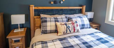 Une chambre à coucher avec une tête de lit en bois, une couvre-lit à carreaux bleus et blancs, et une œuvre d’art abstraite accrochée au mur.