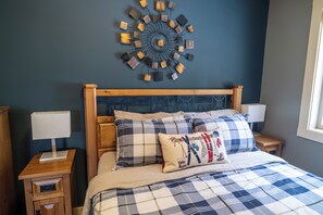 Un dormitorio con cabecera de madera, colcha a cuadros azul y blanco, y una obra de arte abstracta colgada en la pared.