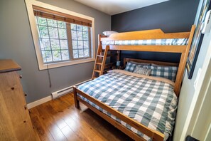 A room with a bunk bed, a window with blinds, a wooden dresser, and a radiator.